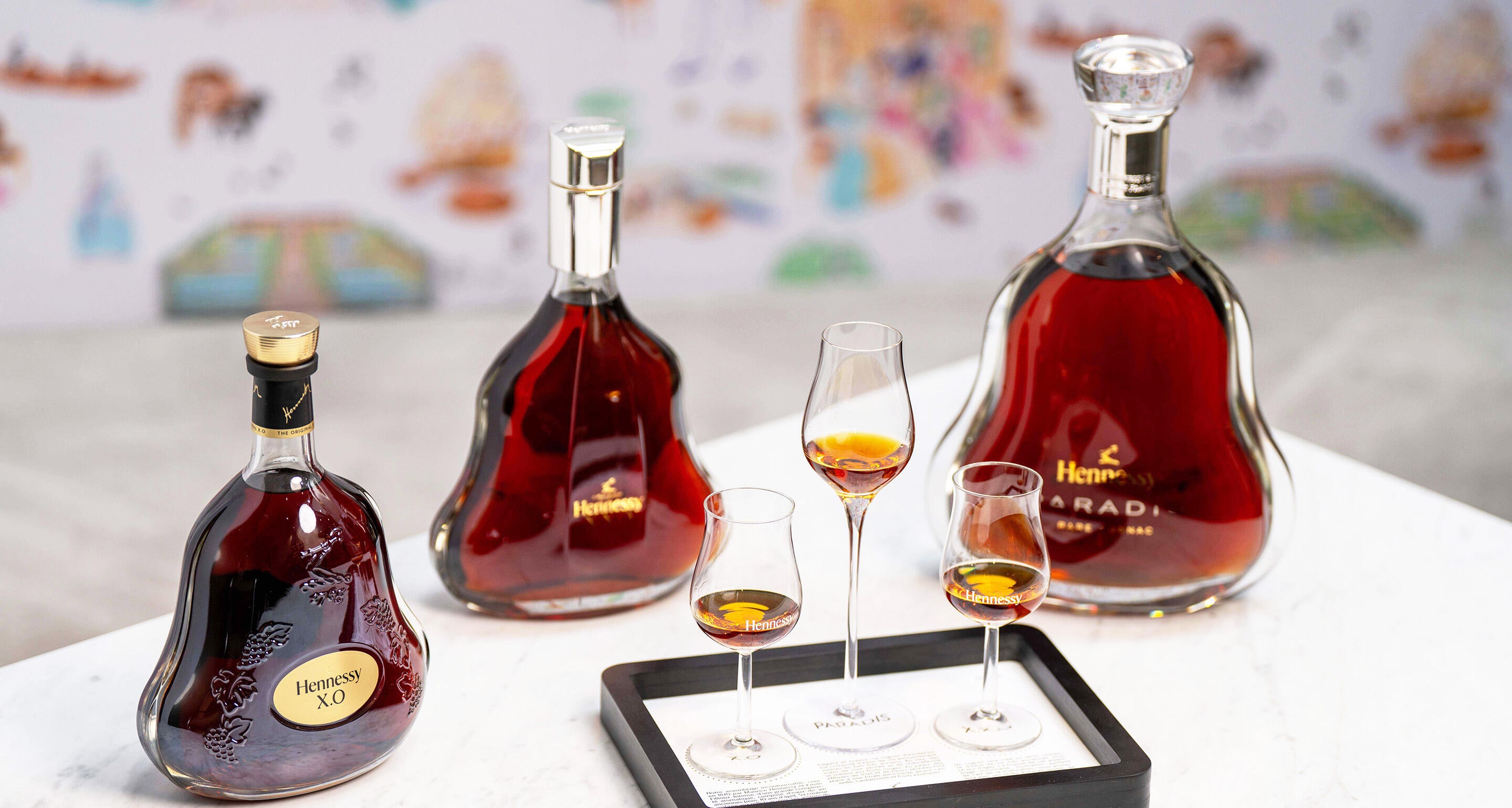 Tasting flight showing 3 different decanters of Hennessy cognacs (Hennessy XO, Hennessy XXO and Hennessy Paradis) on a coffee table, with 3 matches glasses on a service tray