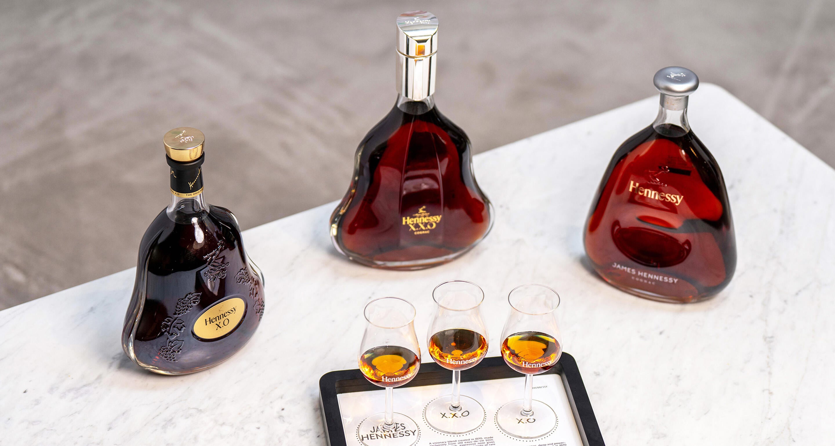 Decanters of James Hennessy, Hennessy X.O and Hennessy X.X.O on a coffee table, with 3 matching glasses of cognac