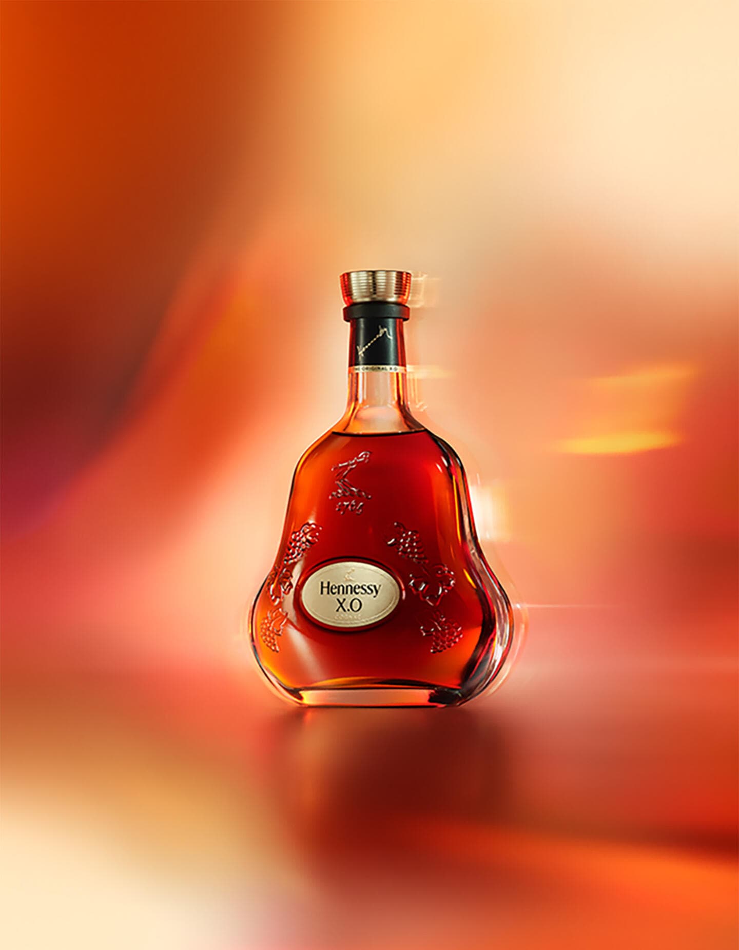 A bottle of Hennessy X.O cognac, set against an artistic red-orange background