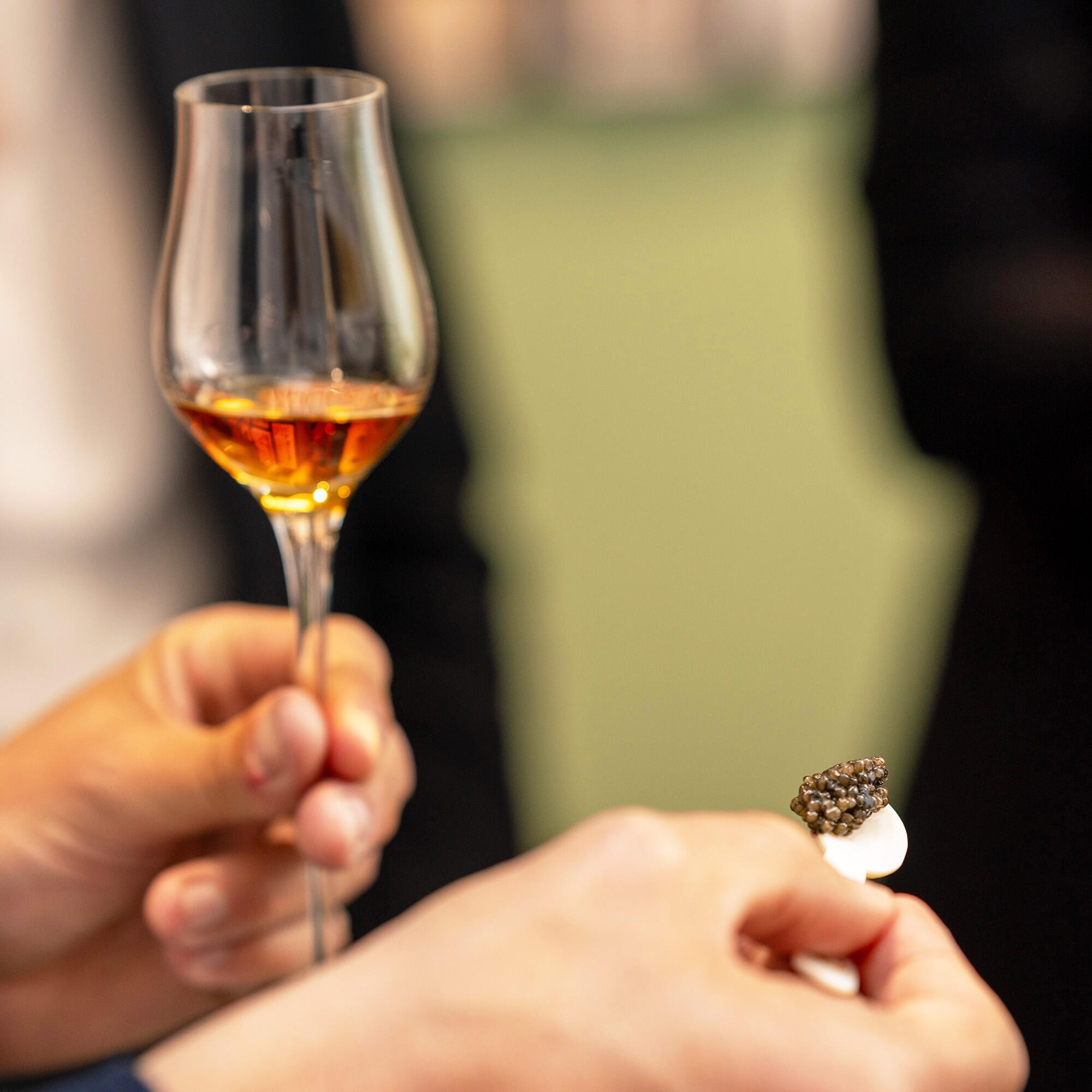 Close-up of a a guest's hand holding a mother-of-pearl spoon, as they are helping themselves to a serving of Prunier Oscietra caviar