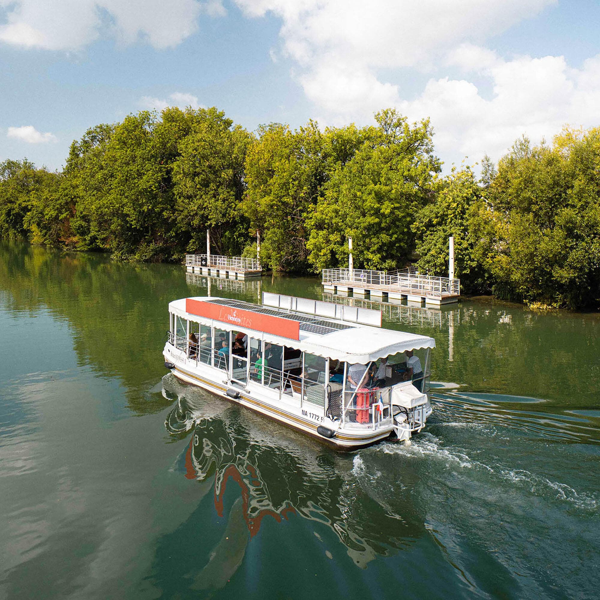 Hennessy solar-powered boat cruising along the Charente River in Cognac, amidst pristine greenery